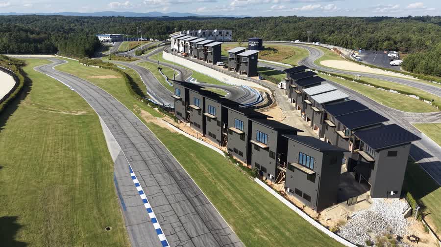 Aerial view of the Circuit Villas clad in dark gunmetal siding, the car circuit running along the near side and the kart circuit behind, with the North Georgia foothills on the horizon