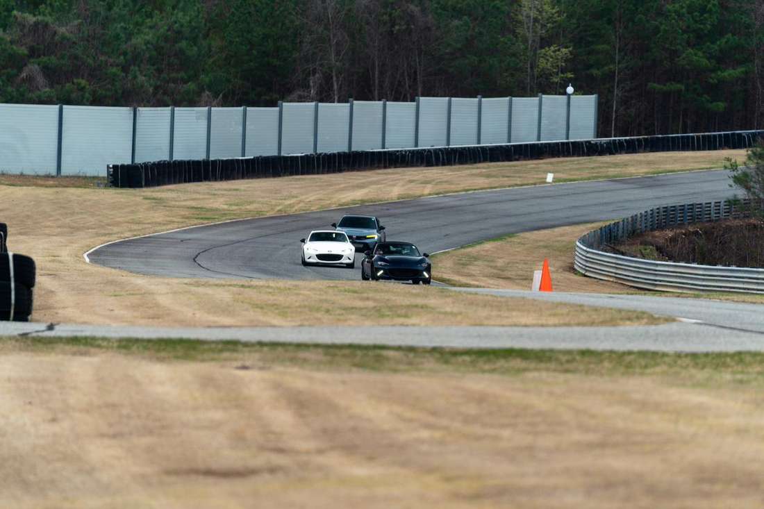 Three cars in line exiting a corner at Atlanta Motorsports Park with the barrier wall and treeline behind